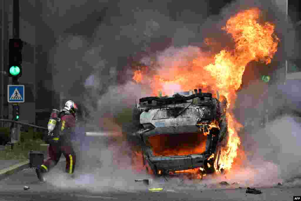 Пожарникар гаси запален автомобил при комеморативниот марш за тинејџер-возач застрелан од полицаец, во париското предградие Нантер.&nbsp;