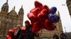 Dos jóvenes que llevan globos con formas de corazón caminan por las calles de la ciudad de Londres, Inglaterra. [Reuters]