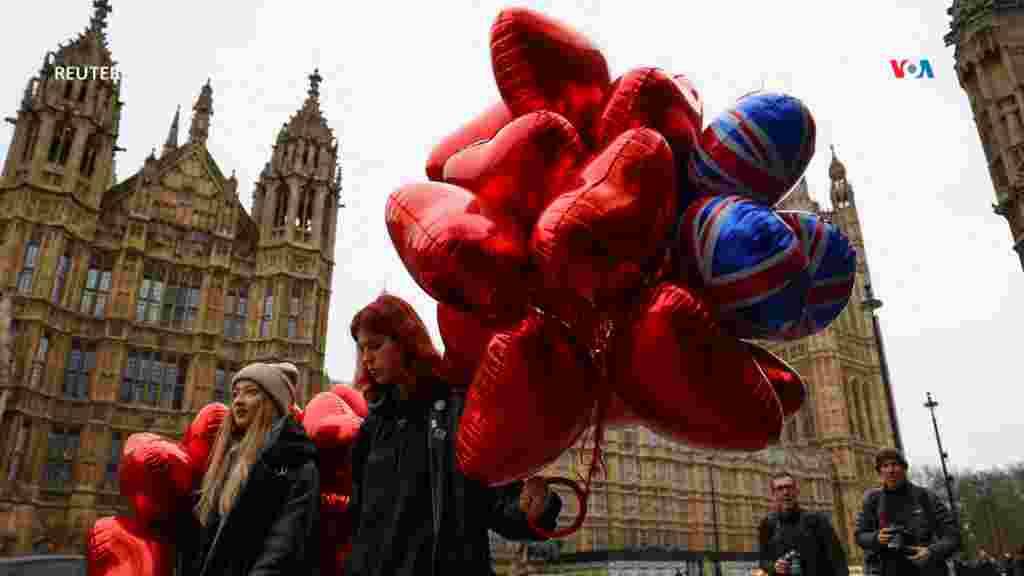 Dos jóvenes que llevan globos con formas de corazón caminan por las calles de la ciudad de Londres, Inglaterra. [Reuters]