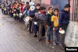 FILE - Palestinian children carry pots as they queue to receive food cooked by a charity kitchen, amid shortages in food supplies, as the conflict between Israel and Hamas continues, in Rafah in the southern Gaza Strip December 14, 2023.