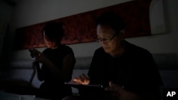 FILE - Wang Quanzhang and his wife, Li Wenzu, look at their phone and laptop in the dark after power was cut off for their apartment in Beijing's Changping district, June 20, 2023.