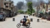 Young men riding a motorbike watch as smoke rises following an explosion allegedly set off by armed insurgents attempting to storm a military compound in Bannu, Pakistan, July 15, 2024. 