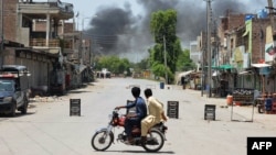 Young men riding a motorbike watch as smoke rises following an explosion allegedly set off by armed insurgents attempting to storm a military compound in Bannu, Pakistan, July 15, 2024. 