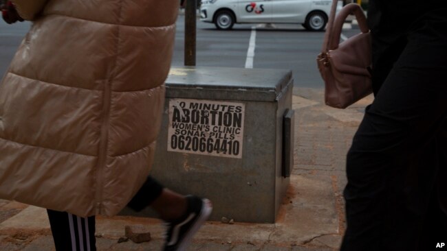 Women pass a sticker advertising abortion pills on a sidewalk in Johannesburg, June 28, 2023.