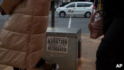 Women pass a sticker advertising abortion pills on a sidewalk in Johannesburg, June 28, 2023.