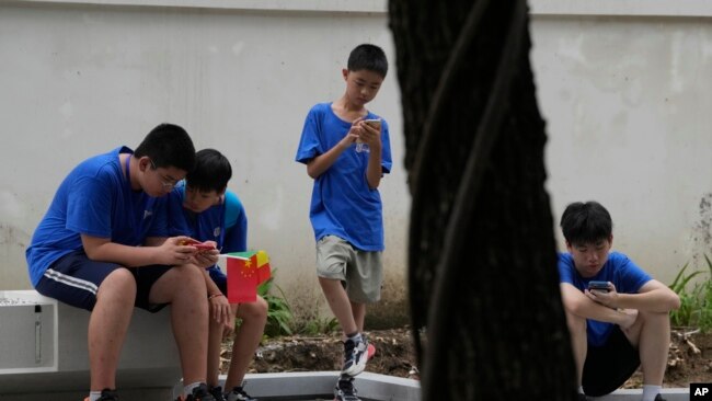 FILE - Youths look at their smartphones on the street in Beijing, Aug. 3, 2023.