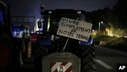A sign on a tractor reads "live simply from our work" at a highway barricade in Aix-en-Provence, southern France, Jan. 30, 2024.