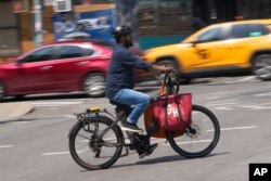 A delivery worker rides a motorized bicycle in New York, Tuesday, July 25, 2023.