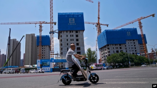 FILE — A man rides by buildings under construction in Beijing, June 5, 2023. The International Monetary Fund says China's economic decline is likely to continue over the next four years.