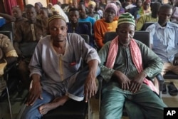 Community members sit in Materi town, Benin, Sunday, Oct. 8, 2023, waiting for a distribution of small portable stoves. (AP Photo/Sam Mednick)