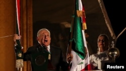 El presidente de México, Andrés Manuel López Obrador, sostiene una campana y la bandera mexicana durante su discurso en el "Grito de Independencia", junto a su esposa Beatriz Gutiérrez Müller, en el Palacio Nacional, en la plaza Zócalo en el centro de la Ciudad de México. 