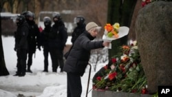 在警察的注视下，一位女士在由第一座苏联古拉格劳改营所在的圣彼得堡由索洛维茨基群岛的巨石建成的纪念碑前敬献鲜花，悼念死在狱中的反对派领袖纳瓦尔尼。(2024年2月17日)