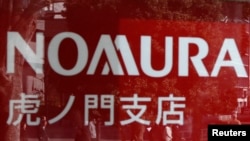 FILE - People are reflected on a window outside a Nomura Securities branch in Tokyo in this 2013 file photo. Charles Wang Zhonghe, China investment banking chairman at Nomura, is prohibited from traveling outside mainland China, sources report.