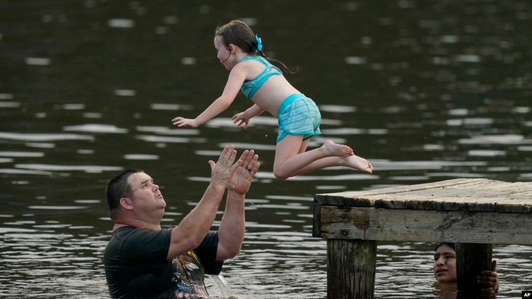 John Crouch membantu seorang anak perempuan berenang untuk mendinginkan tubuh dari cuaca panas di Ross Barnett Reservoir di Bobby Cleveland Park, Lakeshore di Rankin County, Mississippi, Jumat, 30 Juni 2023. (Foto: Rogelio V. Solis/AP)