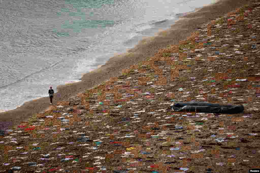 A woman walks at Sant Sebastia beach as Open Arms NGO simulate a scene of a shipwreck to commemorate the lives that were lost after people drowned in the Mediterranean sea in 2023, in Barcelona, Spain.