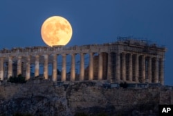 FILE - Bulan purnama muncul di belakang Kuil Parthenon yang berdiri sejak abad ke-5 SM, di bukit kuno Acropolis, Athena, 31 Juli 2023. (AP/Petros Giannakouris, File)