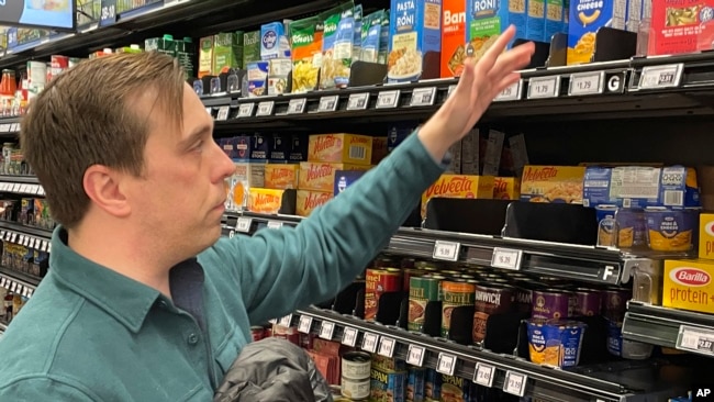 Stuart Dryden reaches for an item at a grocery store on Feb. 21, 2024, in Arlington, Va. Dryden is aware of big price disparities between branded products and their store-label competitors, which he now favors.