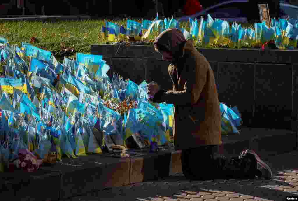 Човек се моли пред импровизиран споменик од украински знамиња со имињата на загинатите војници, на Плоштадот на независноста во Киев, Украина.