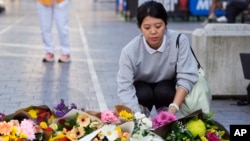 A woman brings flowers to an impromptu memorial at Bondi Junction in Sydney, April 14, 2024, after several people were stabbed to death at a shopping center a day earlier. 