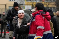 A medical worker helps a woman in a yard of an apartment building destroyed after a Russian attack in Kyiv, Ukraine, Feb. 7, 2024.