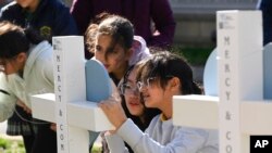 Los niños firman una cruz en la entrada de la Escuela Covenant, el martes 28 de marzo de 2023, en Nashville, Tennessee, que se ha convertido en un monumento a las víctimas del tiroteo escolar del lunes. (Foto AP/John Amis)