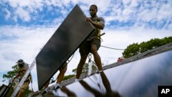 FILE - Employees of NY State Solar, a residential and commercial photovoltaic systems company, install an array of solar panels on a roof, in the Long Island hamlet of Massapequa, New York, Aug. 11, 2022.