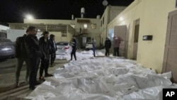 In this image from video, people look over some of the bodies which arrived at Al Aqsa hospital in Deir El Balah, Gaza on Sunday night, Dec. 24, 2023, after three strikes hit Central Gaza.