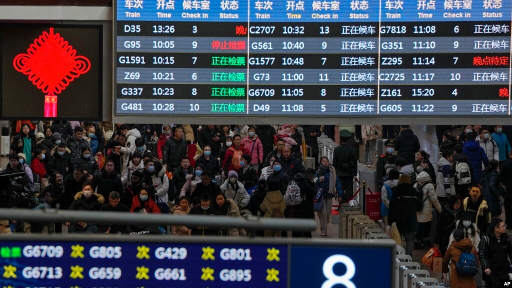 Bagajlı yolcular, trenlerine yetişmek için Batı Tren İstasyonu'na vardıklarında trenin kalkış panosunun altında yürüyor, 7 Şubat 2024, Pekin.