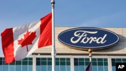 FILE - A Canadian flag flutters in the wind near a Ford logo on the automaker's headquarters, Oct. 26, 2009 in Dearborn, Mich. Canadian autoworkers ratified a new labor agreement with Ford Motor Co., Sept. 24, 2023, averting a threatened strike.