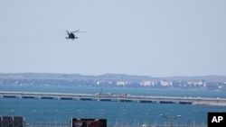 A Russian military helicopter flies over damaged parts of an automobile link of the Crimean Bridge connecting the Russian mainland and the Crimean peninsula over the Kerch Strait on July 17, 2023. (AP Photo)