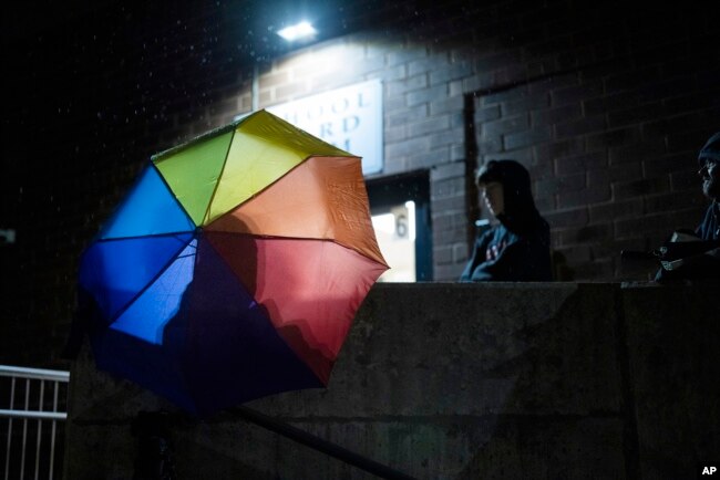 FILE - Central Bucks School District high school student Leo Burchell waits for a school board meeting to start, opening his rainbow colored umbrella as it begins to rain in Doylestown, Pa., on Tuesday, Nov. 15, 2022.(AP Photo/Ryan Collerd)