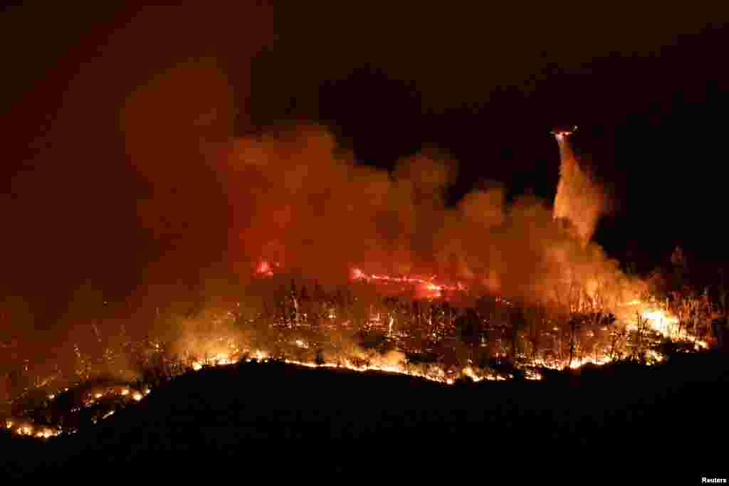 A helicopter drops water over the Thompson wildfire as firefighters continue battling fire into the night near Oroville, California, July 2, 2024. 