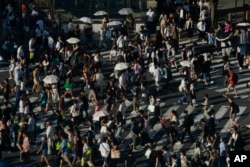 People carry umbrellas to shield themselves from the sun as they walk across an intersection July 17, 2023, in Tokyo.