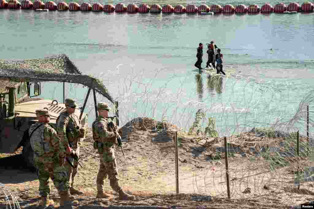 Asylum-seeking migrants walk in the Rio Grande River as they look for an opening in a concertina wire fence so they can get to U.S. soil, in Eagle Pass, Texas, July 24, 2023.