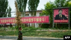 FILE - A woman passes by a portrait of Chinese President Xi with a slogan urging people to 'struggle unremittingly to realize the Chinese dream of the great rejuvenation of the Chinese people', near Yarkant, Xinjiang region, July 16, 2023.