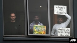 FILE - Three asylum seekers gesture to protesters rallying outside in their support, from their hotel room where they have been detained in Melbourne, Australia, June 13, 2020.