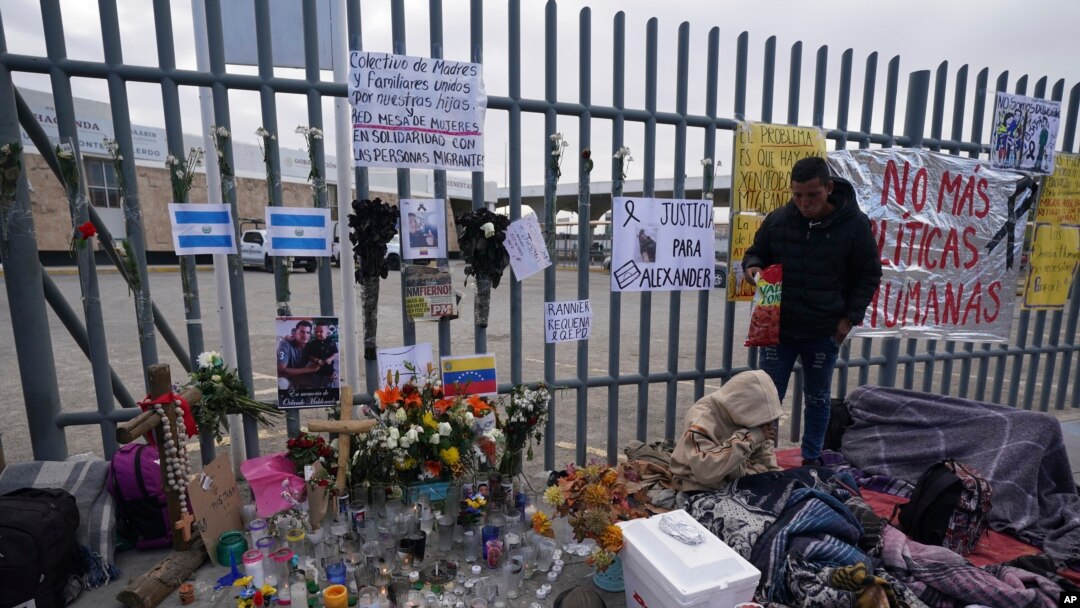 Un altar con velas y fotos cubre la cerca afuera del centro de detención de migrantes que fue el sitio de un incendio mortal, mientras los migrantes se despiertan después de pasar la noche en la acera en Ciudad Juárez, México, el jueves 30 de marzo de 2023.