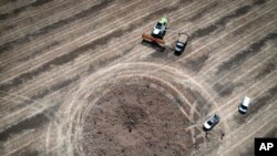 FILE - A farmer harvesting a field 10 km from the front line, maneuvers around a crater left by a Russian rocket in the Dnipropetrovsk region, Ukraine, July 4, 2022.