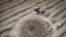 FILE - A farmer harvesting a field 10 km from the front line, maneuvers around a crater left by a Russian rocket in the Dnipropetrovsk region, Ukraine, July 4, 2022.