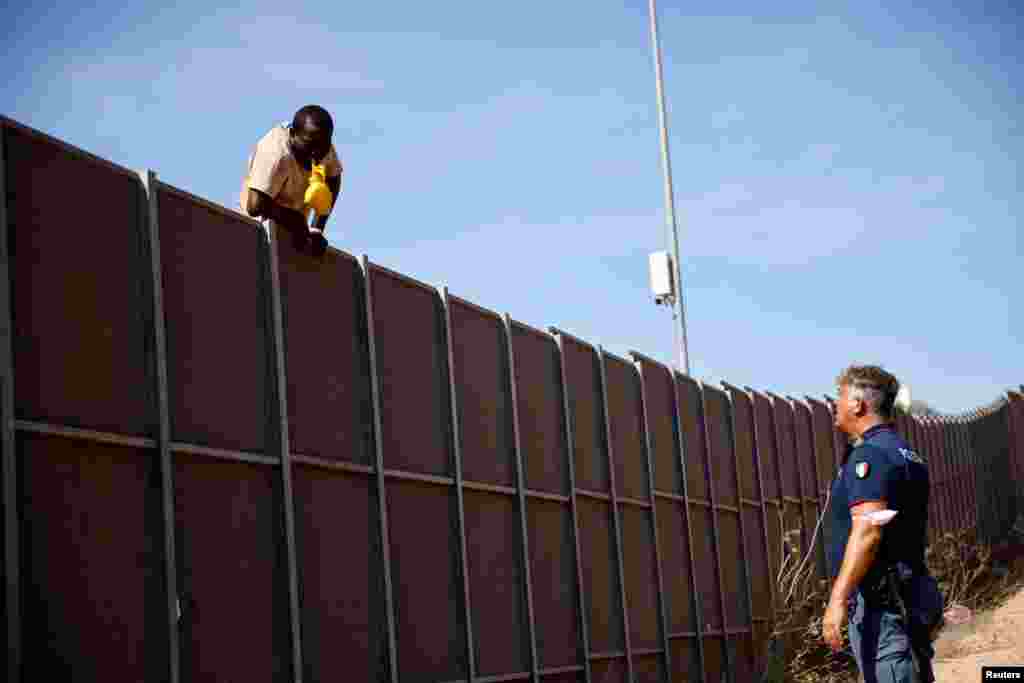 Полицаец разговара со мигрант кој се обидува да побегне од жариштето, на сицилијанскиот остров Лампедуза, Италија.