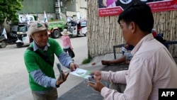 In this photo taken on July 4, 2023, a member (L) of Cambodia's Grassroots Democratic Party (GDP) distributes political campaign leaflets during the general election campaign in Phnom Penh.