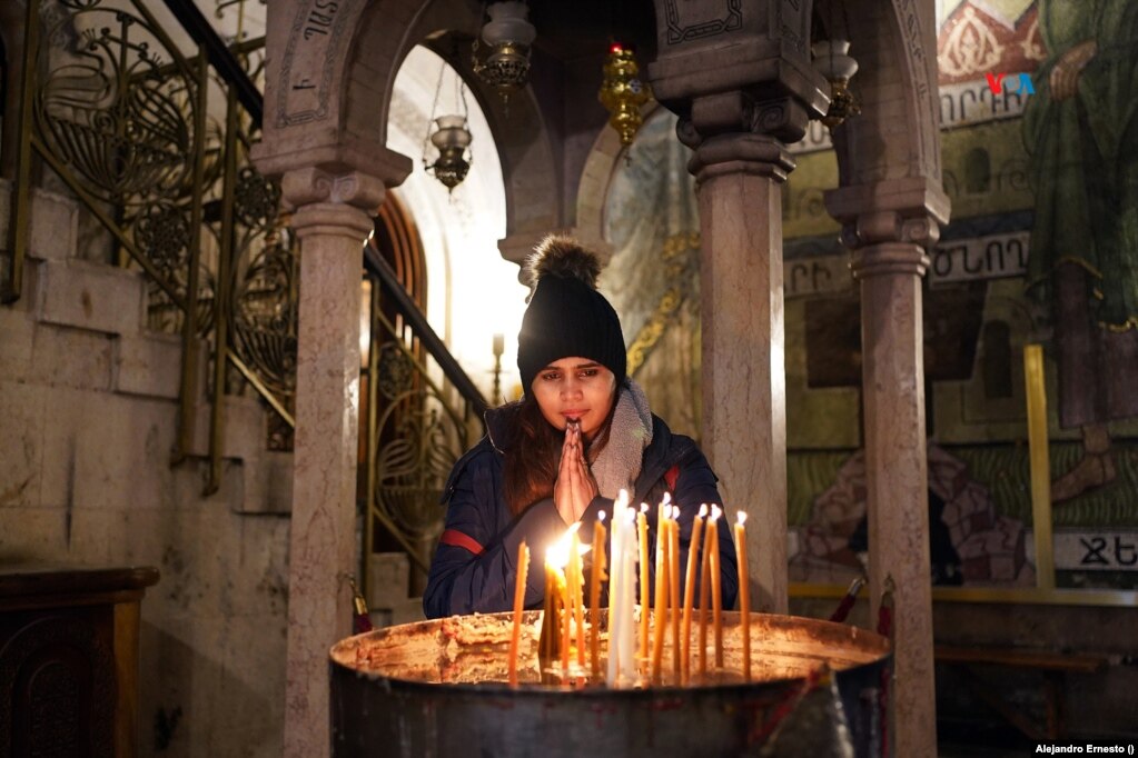 Una joven cristiana reza frente a unas velas en la entrada del Santo Sepulcro de Jerusalén, muy cerca del Edículo, donde supuestamente Jesús resucitó y subió al cielo y donde se conserva su tumba.