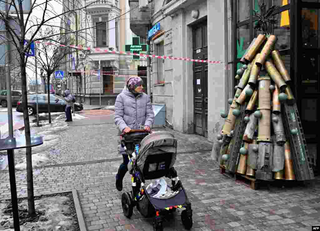 A woman pushes a stroller as she walks past a symbolic Christmas tree made from spent shells casing and other spent ammunition erected outside a cafe in the center of Kyiv, Ukraine, Dec. 18, 2023.