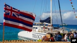 FILE - Tourists get off of a Trilogy Excursions boat arriving on Kaanapali Beach in front of a flag of Hawaii planted in the sand, Dec. 6, 2023, in Lahaina, Hawaii.