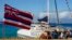 FILE - Tourists get off of a Trilogy Excursions boat arriving on Kaanapali Beach in front of a flag of Hawaii planted in the sand, Dec. 6, 2023, in Lahaina, Hawaii.