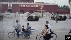 ARCHIVO - Ciclistas pasan junto a vehículos blindados estacionados frente a la Puerta de Tiananmen, cerca de la plaza donde los estudiantes se manifestaron por reformas democráticas en Beijing, el 13 de junio de 1989.