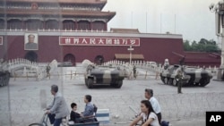 FILE - Cyclists pass by armored vehicles parked in front of Tiananmen Gate near the square where students rallied for democratic reforms in Beijing, June 13, 1989.
