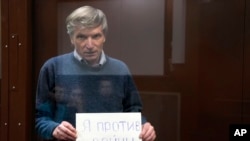 FILE - Alexei Gorinov holds a sign reading 'I am against the war' as he stands in a cage during hearing in the courtroom in Moscow, on June 21, 2022.