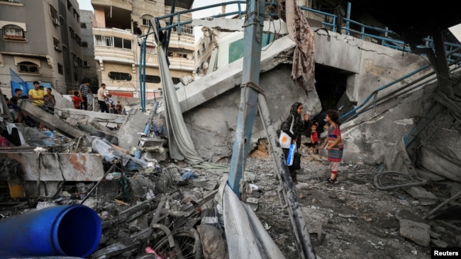 Warga Palestina berdiri di tengah puing-puing sekolah milik PBB yang menampung para pengungsi, menyusul serangan Israel, di tengah konflik Israel-Hamas, di Kota Gaza, 18 Juli 2024. (Foto: Dawoud Abu Alkas/Reuters)