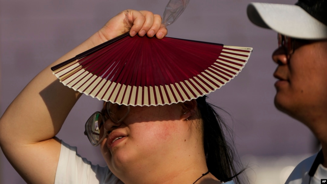 Seorang perempuan menggunakan kipas miliknya untuk menghindari terpaan sinar matahari saat ia berjalan di tengah cuaca panas di Beijing, pada 16 Juni 2024. (Foto: AP/Andy Wong)